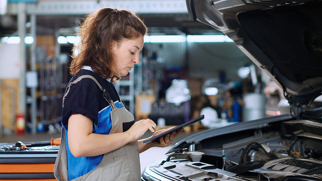 Technician matching a vehicle VIN on a tablet to a genuine OEM part in its factory box at a parts counter