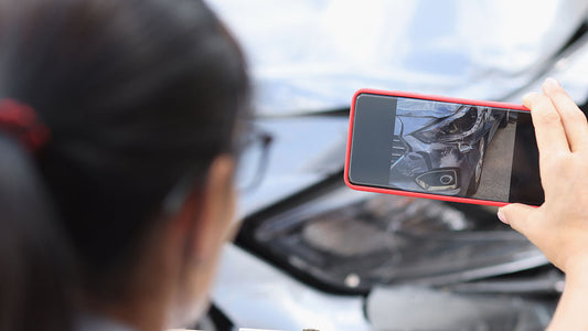 An insurance adjuster photographing the damaged front corner of a car in a parking lot to write a quick first estimate