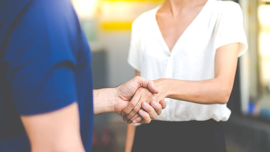 A customer shaking hands with a service advisor next to a clean loaner car outside an auto repair shop on a sunny day