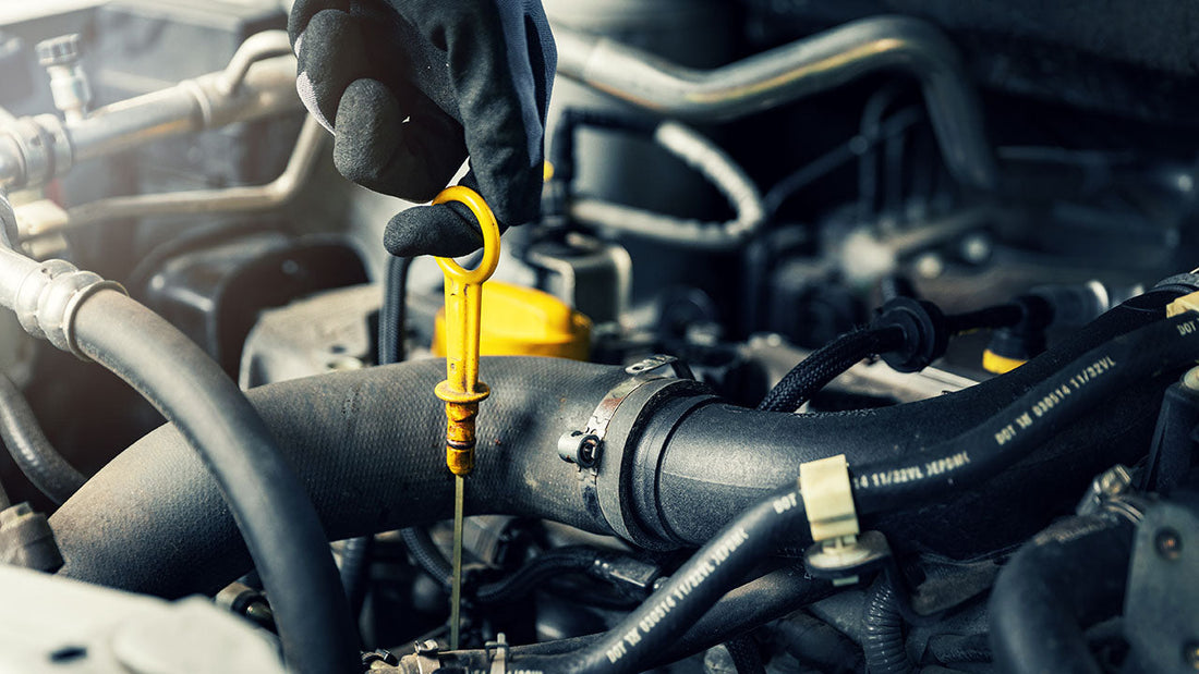 A person pulling the oil dipstick to check engine oil level in a car engine bay
