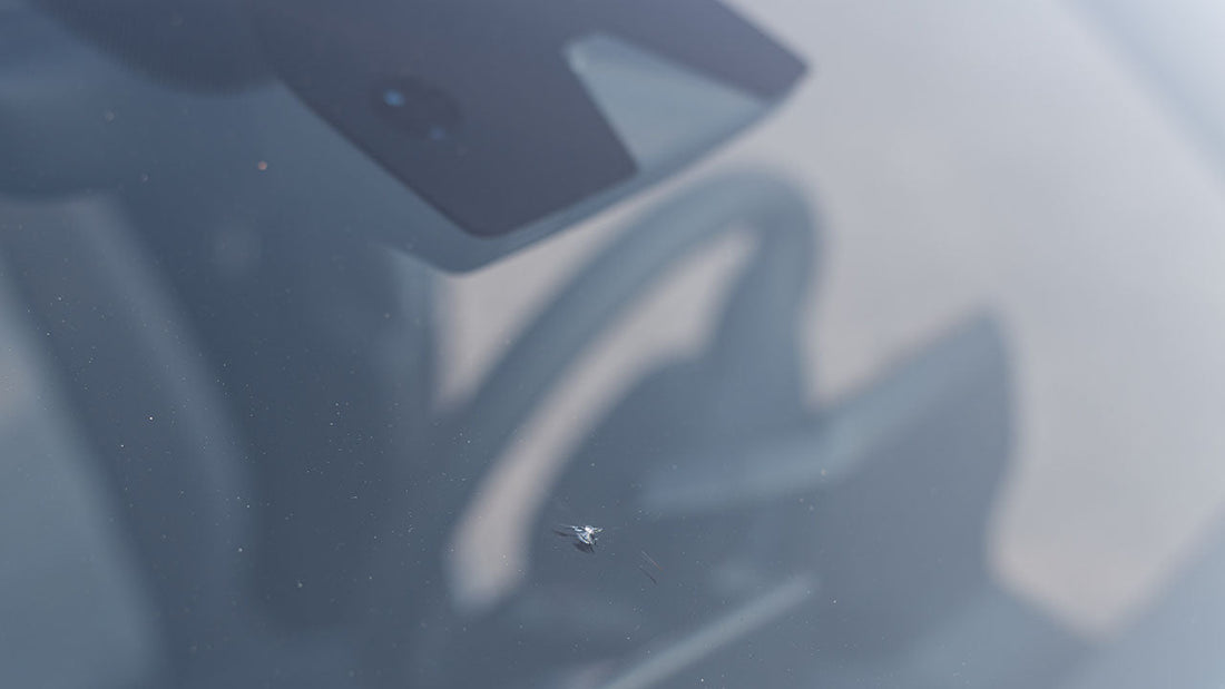 A cracked windshield with the small ADAS camera module visible behind the glass near the rearview mirror