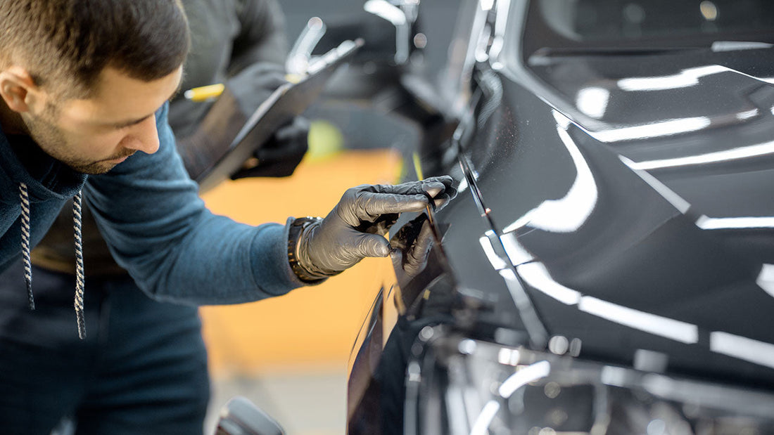 A technician inspecting damaged structure behind a removed front bumper cover, photographing parts that were hidden on the first estimate