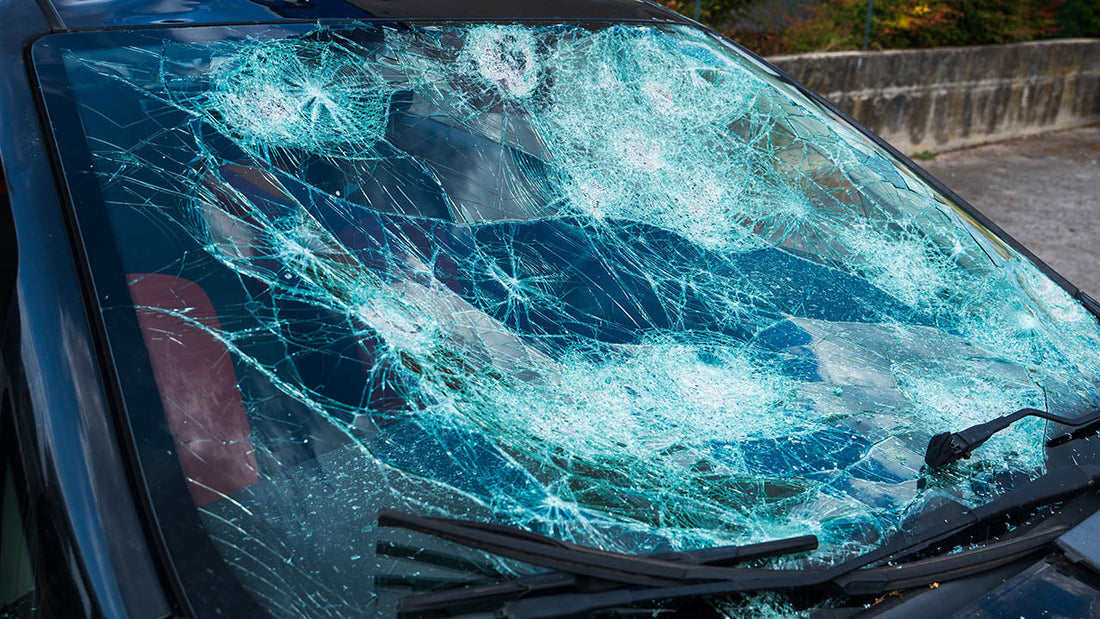 A car parked on a residential Los Angeles street showing fresh hail dents on the door panel and hood and a cracked windshield under clearing storm clouds