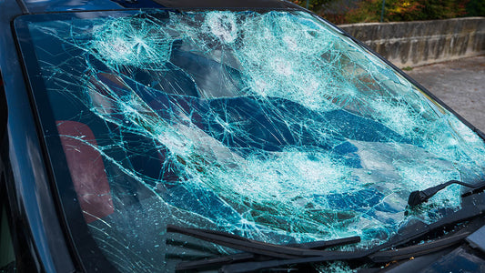 A car parked on a residential Los Angeles street showing fresh hail dents on the door panel and hood and a cracked windshield under clearing storm clouds