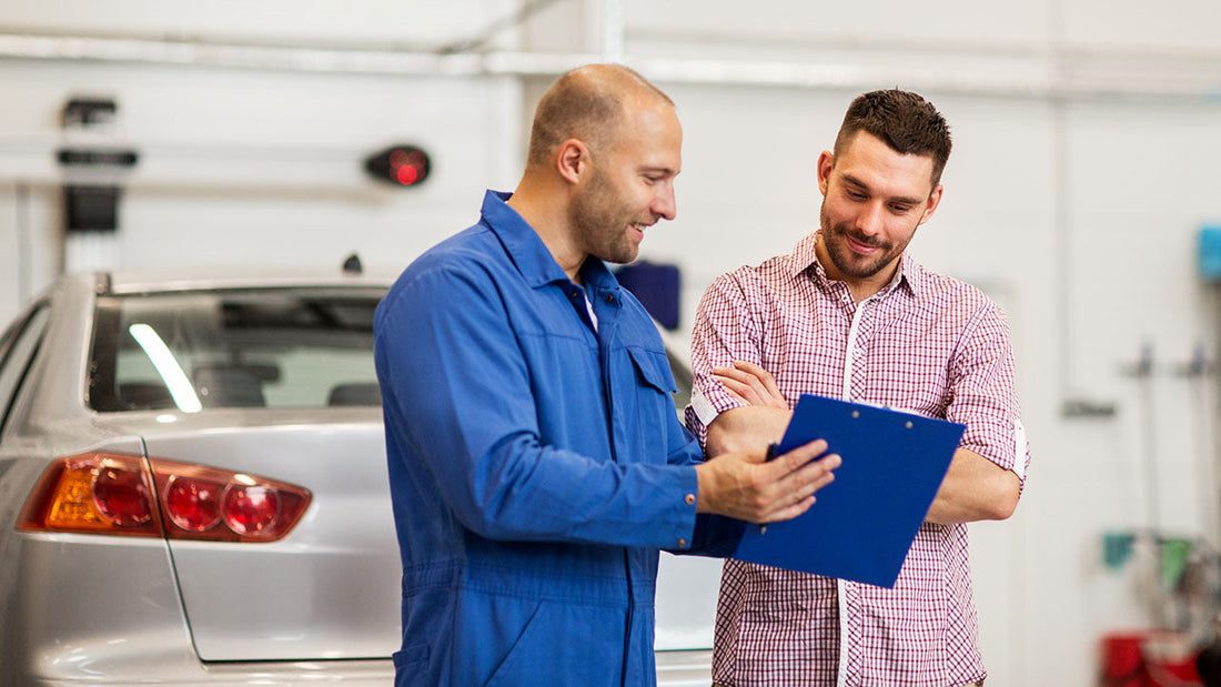 A collision shop estimator reviewing a single written repair estimate with a car owner beside a damaged vehicle